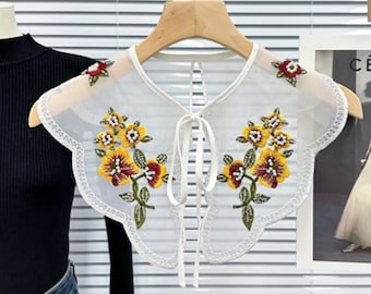 May include: White sheer lace collar with a scalloped edge and floral embroidery. The embroidery features yellow, red, and white beads. The collar has a tie at the back.