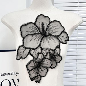 May include: Black floral applique with a large hibiscus flower and two smaller flowers. The applique is made of sheer fabric with black embroidery.