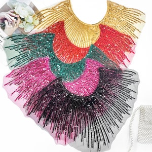May include: Four sequined fabric trims in different colours. The trims are layered on top of each other, with the gold trim on top. The trims are shaped like a half-circle and have a fringe design.