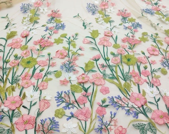 May include: A delicate floral embroidered tulle fabric with pink, white, green, and blue flowers. The fabric is perfect for crafting, sewing, and creating unique projects.