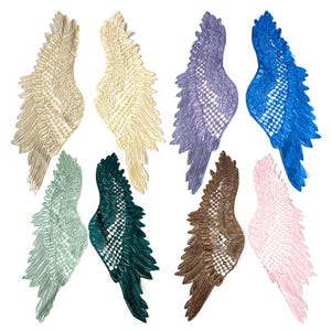 May include: A selection of lace angel wing appliques in a variety of colours. The wings are presented in pairs, with shades including cream, lavender, blue, green, brown, and pink. Each wing has a detailed, openwork design.