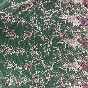 May include: Delicate floral lace fabric in a soft pink and white color scheme. The design features embroidered branches with small pink flower accents and a scalloped edge. This fabric is ideal for bridal wear or other special occasion garments.