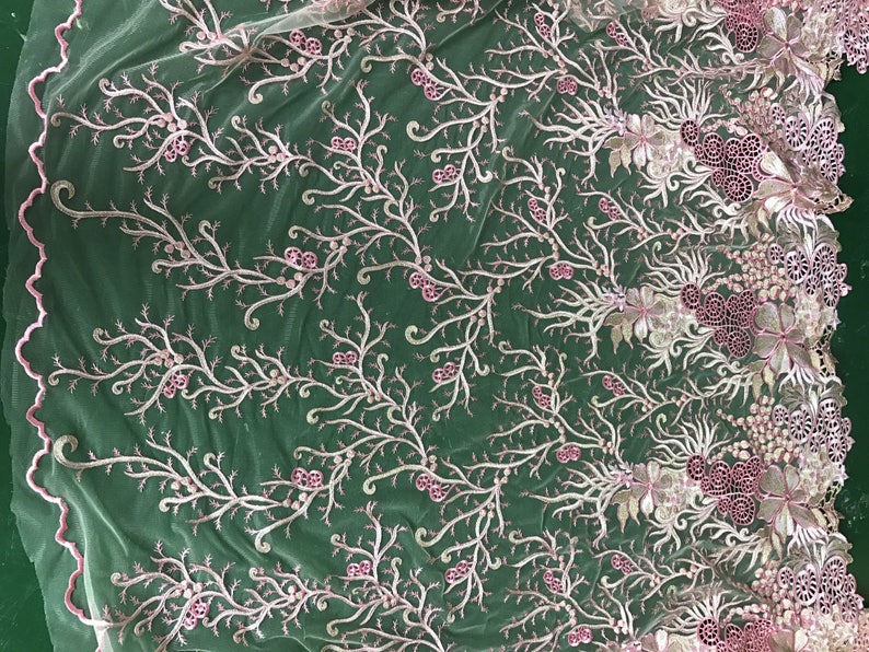 May include: Delicate floral lace fabric in a soft pink and white color scheme. The design features embroidered branches with small pink flower accents and a scalloped edge. This fabric is ideal for bridal wear or other special occasion garments.