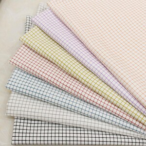 May include: A selection of fabric swatches in a range of colours, such as peach, lavender, yellow, red, blue, grey, and black. Each fabric features a grid pattern, forming a checkered design. The fabrics are arranged to display the colour variations.