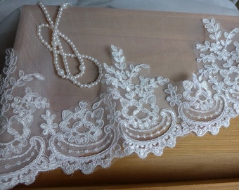 May include: White lace trim with a delicate floral pattern. The lace is on a sheer, beige fabric.