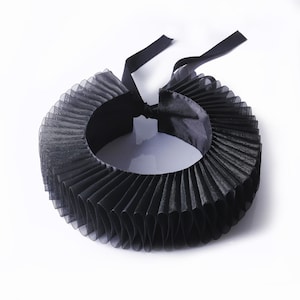 Könnte beinhalten: Ein schwarzer, plissierter Kragen mit einem mehrschichtigen Design. Der Kragen besteht aus einem transparenten Stoff und hat hinten eine Satinbandschleife. Der Kragen ist ein Modeaccessoire, geeignet für Cosplay oder Kostümzwecke.