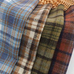 May include: Close-up of four different plaid fabric swatches. The fabrics feature a variety of colors, including blue, brown, green, and red. The plaid patterns are detailed and the fabrics appear to be soft and textured.