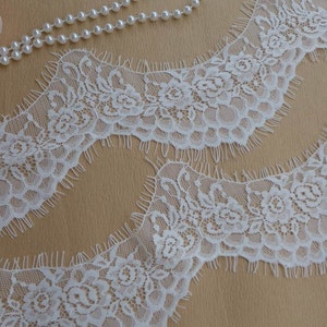 May include: White lace trim with a scalloped edge and floral design. The lace has a frayed edge.