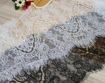 May include: Two pieces of lace trim, one white and one black, with a delicate floral pattern. The lace is soft and flowing, with a frayed edge.