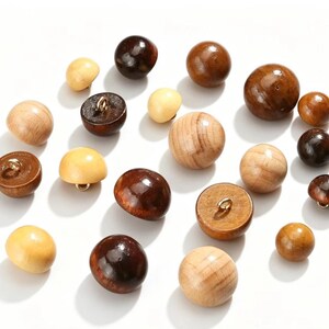 Pode incluir: Uma coleção de botões de madeira redondos em vários tons de castanho, variando do bege claro ao espresso escuro. Cada botão apresenta um acabamento liso e polido e um pequeno gancho metálico na parte inferior para fixação em tecidos.