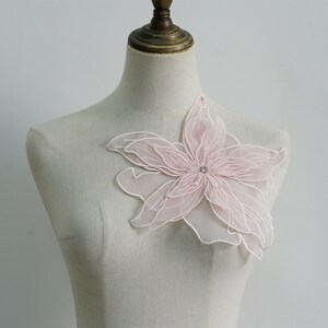 May include: A delicate pink flower applique with a rhinestone center. The applique is made of layered tulle and is perfect for adding a touch of elegance to any garment.