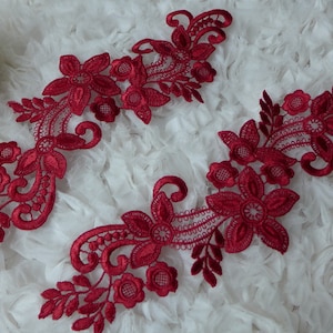 May include: Two red lace appliques with floral designs. The appliques are made of delicate lace and feature intricate floral patterns.