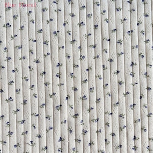 May include: Cream-colored ribbed fabric with a repeating pattern of small blue floral sprigs. The text "Blue Floral" is in the upper left corner. The fabric has a vertical ribbed texture.