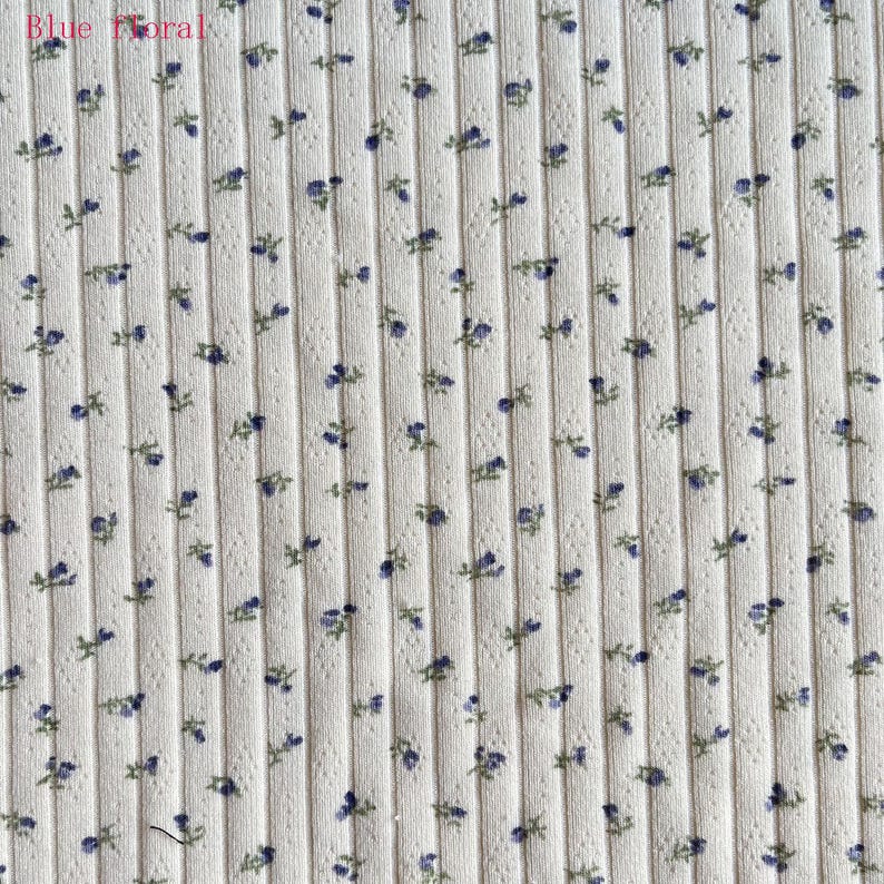 May include: Cream-colored ribbed fabric with a repeating pattern of small blue floral sprigs. The text "Blue Floral" is in the upper left corner. The fabric has a vertical ribbed texture.