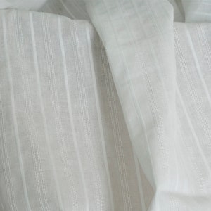 May include: White cotton fabric with vertical stripes. The fabric is sheer and has a slightly textured surface.