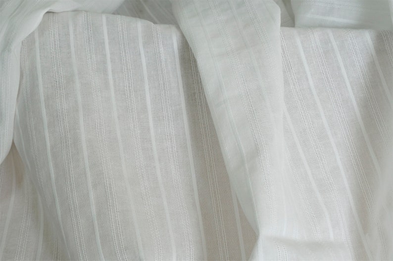 May include: White cotton fabric with vertical stripes. The fabric is sheer and has a slightly textured surface.