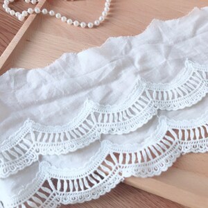 May include: White cotton lace trim with scalloped edges and a delicate crochet pattern. The lace has a layered design with two rows of scallops.