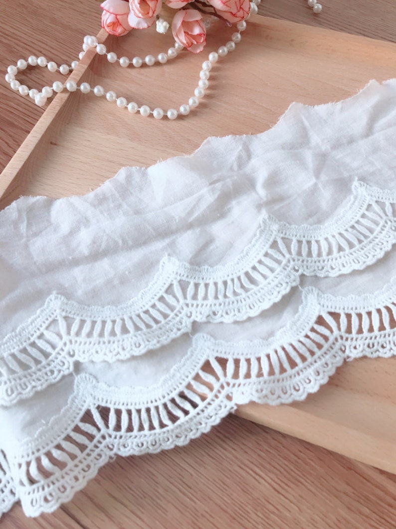 May include: White cotton lace trim with scalloped edges and a delicate crochet pattern. The lace has a layered design with two rows of scallops.