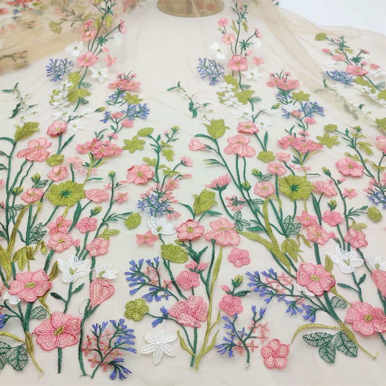 May include: A delicate floral embroidered tulle fabric with pink, white, green, and blue flowers. The fabric is perfect for crafting, sewing, and creating unique projects.