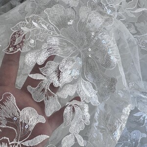 May include: White floral lace fabric with sequins. The lace features a delicate floral pattern with a sheer mesh background.