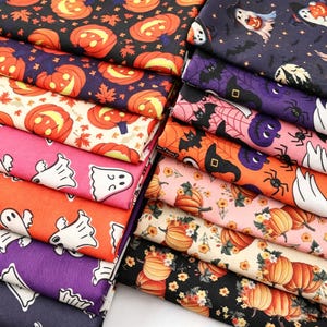 May include: A collection of folded fabric squares featuring various Halloween-themed patterns including orange jack-o'-lanterns, white ghosts, black bats, purple spiders, and floral pumpkin designs on black, orange, pink, and cream backgrounds.