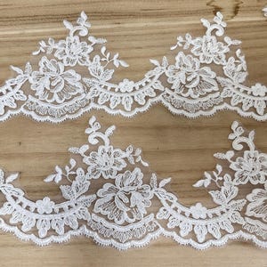 May include: Close-up of white floral lace trim. The lace features a repeating pattern of flowers, leaves, and scalloped edges. The delicate design is set against a sheer background, ideal for bridal or craft projects.