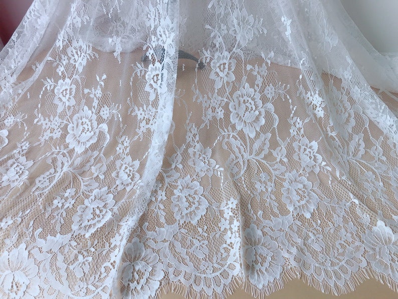 May include: White lace fabric with a floral pattern. The lace has a scalloped edge.