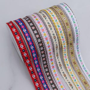Op de afbeelding: Een selectie van decoratieve linten in verschillende kleuren, elk met een bloemenpatroon langs de randen. De linten zijn opgerold en getoond, waarbij de verschillende kleurencombinaties en ontwerpen worden getoond. Ideaal voor knutselen en versieringen.
