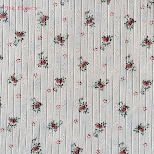 May include: Cream-colored fabric with a ribbed texture and a repeating floral pattern. The pattern features clusters of red roses with green leaves and small red dots. The words "Pink flowers" are in the top left corner.