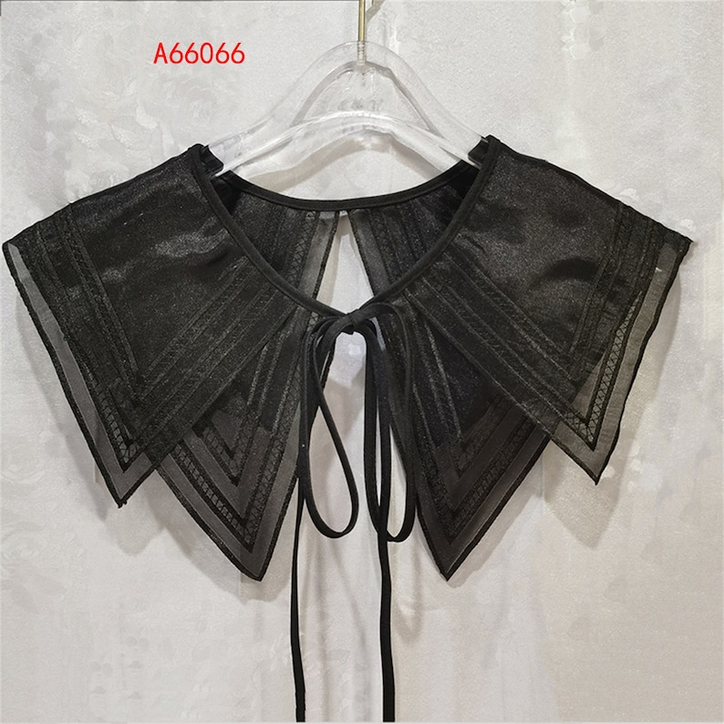 May include: A black sheer lace collar with a tie closure. The collar has a layered design with a scalloped edge.
