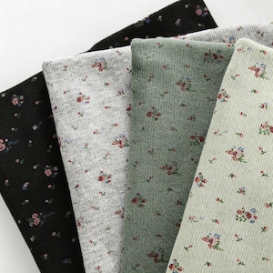 Pu&ograve; includere: Primo piano di quattro campioni di tessuto in nero, grigio, verde e verde chiaro. Ogni campione presenta un motivo floreale con piccoli fiori rossi e blu. Il tessuto ha una trama a coste.