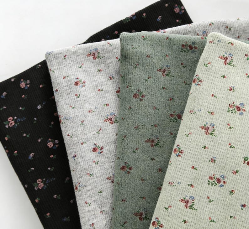 Pu&ograve; includere: Primo piano di quattro campioni di tessuto in nero, grigio, verde e verde chiaro. Ogni campione presenta un motivo floreale con piccoli fiori rossi e blu. Il tessuto ha una trama a coste.