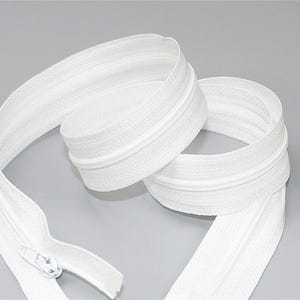 May include: A coiled white zipper with a white pull tab. The zipper tape is a bright white color, and the zipper teeth are also white. The zipper is shown against a light gray background.