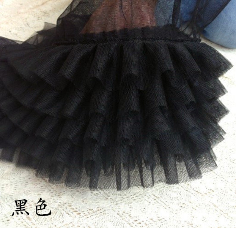 May include: Black tulle fabric with multiple layers of ruffles. The fabric is soft and delicate, and the ruffles are evenly spaced.