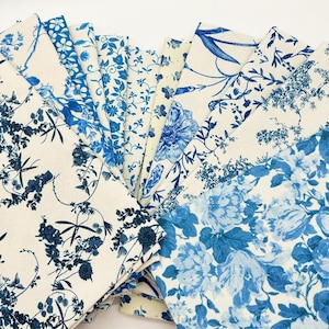 May include: A selection of folded fabric samples showcasing diverse blue floral designs against a cream backdrop. The patterns depict detailed botanical illustrations of flowers, leaves, and vines, offering a classic, elegant look. The fabrics are arranged in a fan shape.