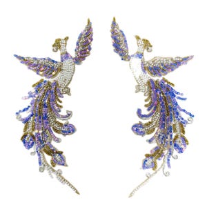 May include: A pair of mirror-image phoenix bird appliques featuring intricate beadwork and sequins. The birds are decorated in shades of white, purple, blue, and metallic gold, with long, flowing tail feathers extending downwards in a curved design.