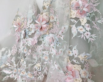 May include: Delicate floral lace fabric with 3D pink flowers and pearl embellishments. The lace is on a sheer, light blue background.