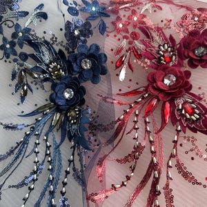 May include: Close-up of two embroidered floral appliques. One is navy blue with silver and clear accents, the other is burgundy with red and clear accents. Both feature sequins, beads, and crystal-like embellishments on a sheer mesh backing.