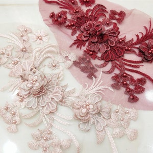 Può includere: Due delicati ricami in pizzo floreale con decorazioni di perle. Un ricamo è rosa e l'altro è bordeaux.