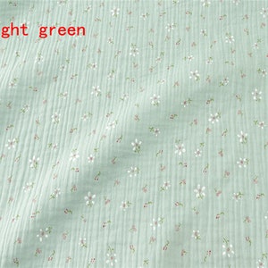 May include: Light green fabric with a small white floral pattern. The fabric has a slightly textured surface.