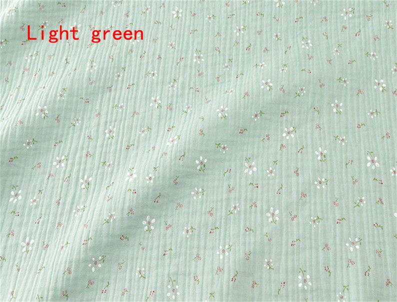 May include: Light green fabric with a small white floral pattern. The fabric has a slightly textured surface.