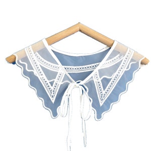 May include: A white lace collar with a scalloped edge and a tie closure. The collar is made of sheer fabric and has a delicate, feminine look.