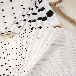 May include: A collection of white fabric swatches featuring various black polka dot patterns, ranging from large, scattered circles to fine, dense dots, arranged in a fan-like display to showcase the different scales of the printed designs.