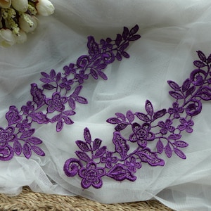 Puede incluir: Dos aplicaciones de encaje morado con diseños florales y de hojas. Las aplicaciones están sobre un fondo blanco.