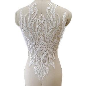 May include: White lace applique featuring a floral design. The lace is delicate and intricate, with a variety of different shapes and sizes of flowers. The applique is ideal for adding a touch of elegance to any garment.