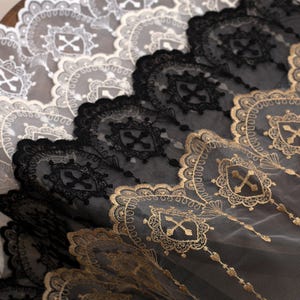 May include: Close-up of decorative lace fabric in black, gold, and white. The lace features an intricate design with repeating patterns of crosses and ornate borders. The fabric is layered, showcasing the different colors and textures.