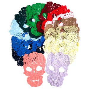 May include: A collection of skull-shaped lace appliques in various colors including dark green, bright green, maroon, red, white, brown, beige, yellow, light blue, royal blue, black, coral, and lavender, arranged in a circular pattern.
