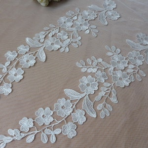 Może przedstawiać: Dwa kawałki białej koronki kwiatowej o delikatnym wzorze. Koronka wykonana jest z cienkiej siateczki z małymi kwiatami i liśćmi.