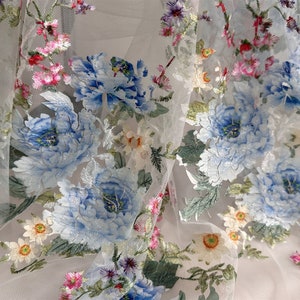 Puede incluir: Tela de tul blanco con patrones florales bordados en azul y verde. Las flores son grandes y detalladas, con un efecto delicado, casi como de acuarela.