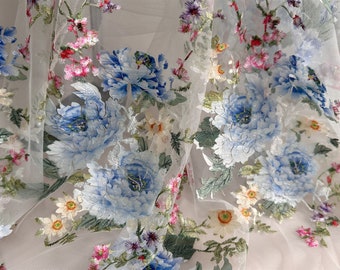 May include: White tulle fabric with embroidered blue and green floral patterns. The flowers are large and detailed, with a delicate, almost watercolor-like effect.